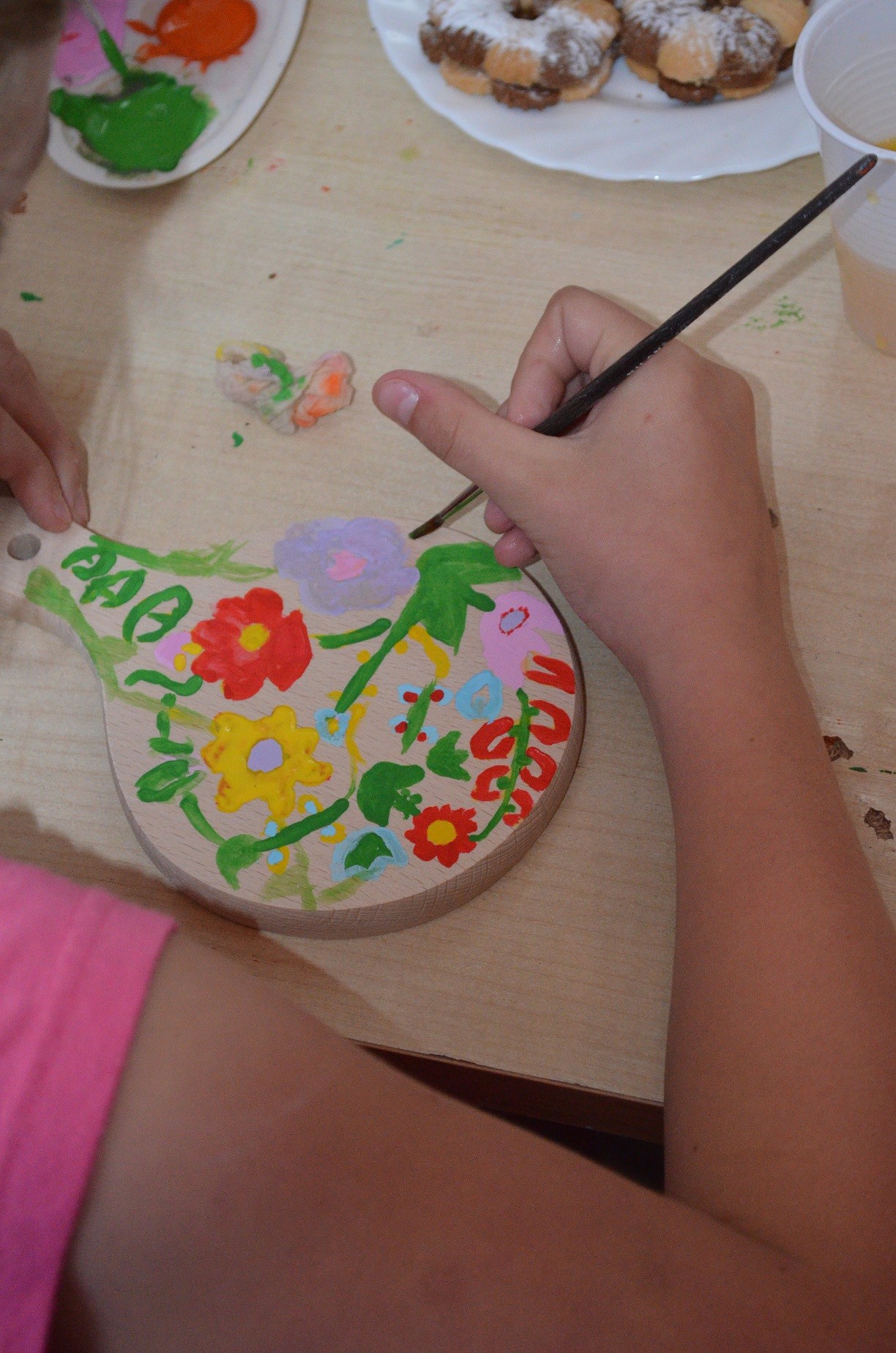 Ręka malująca kwiaty na drewnianej deseczce.